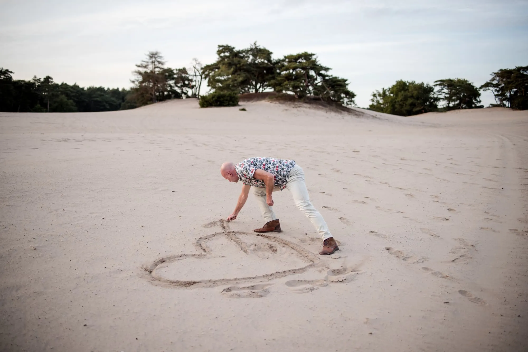 Hij tekent lachend een hart in het zand terwijl zij toekijkt