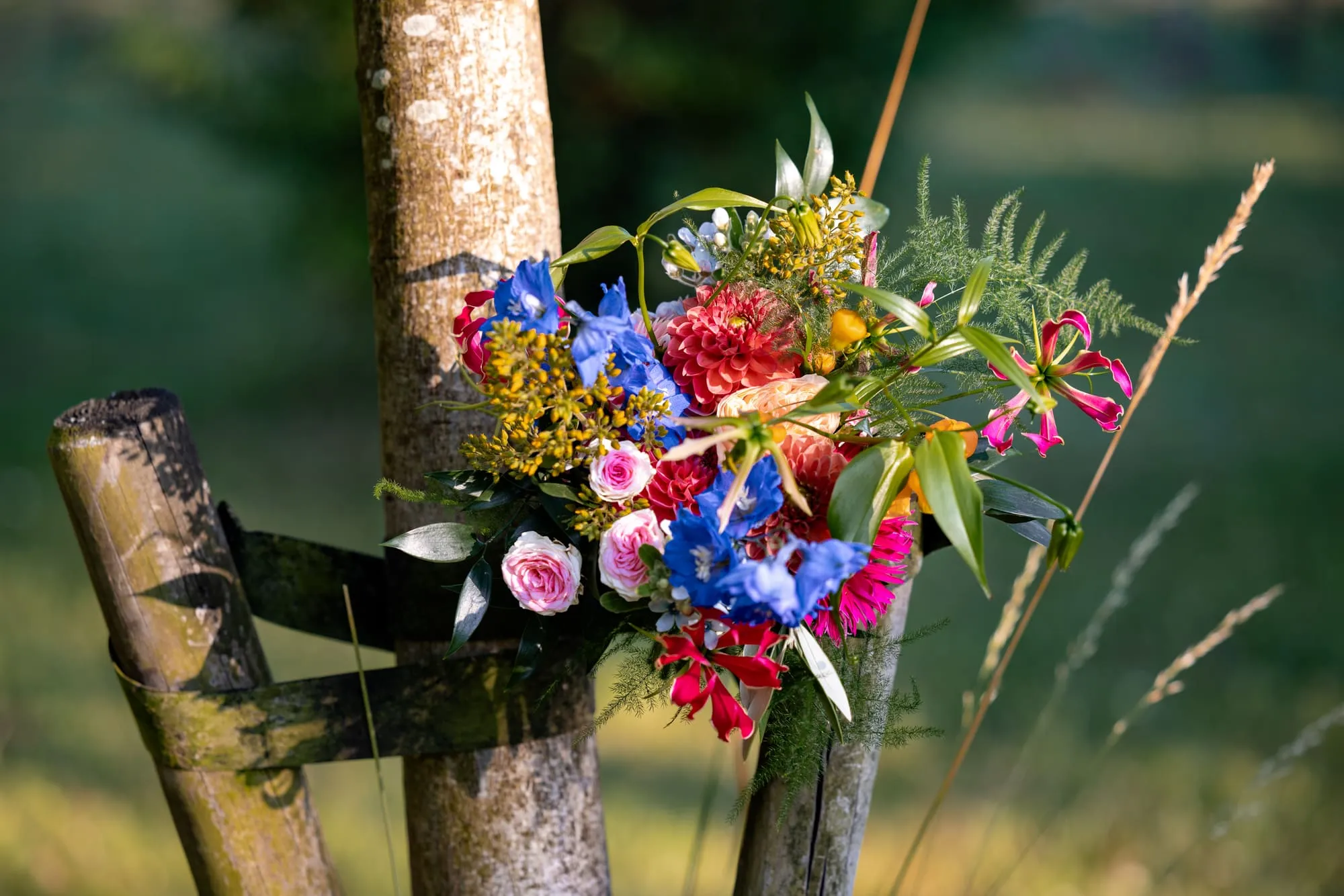 Een kleurrijk bloemstuk aan een houten paal in het veld