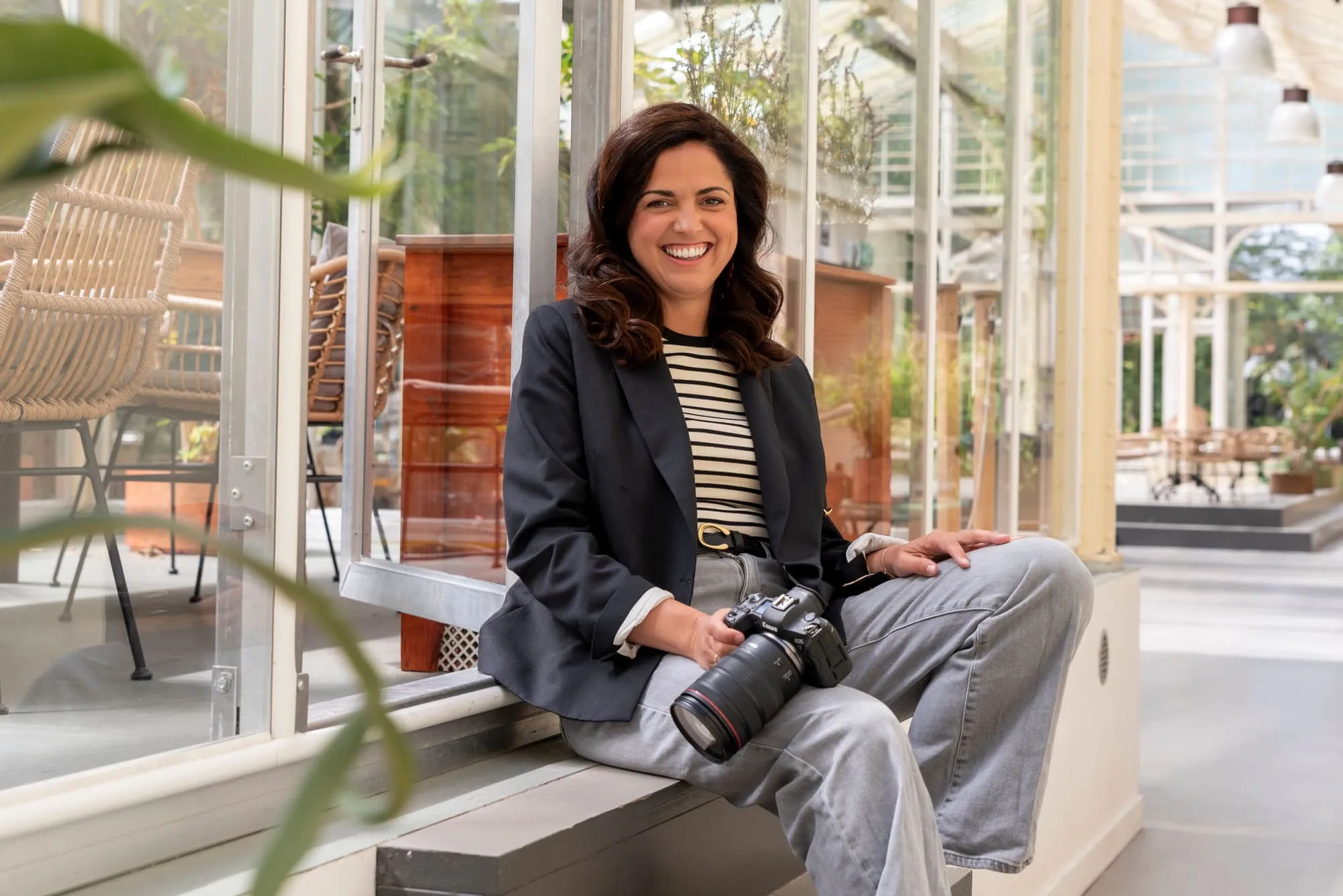 Françoise zit lachend met haar camera in een kas vol planten