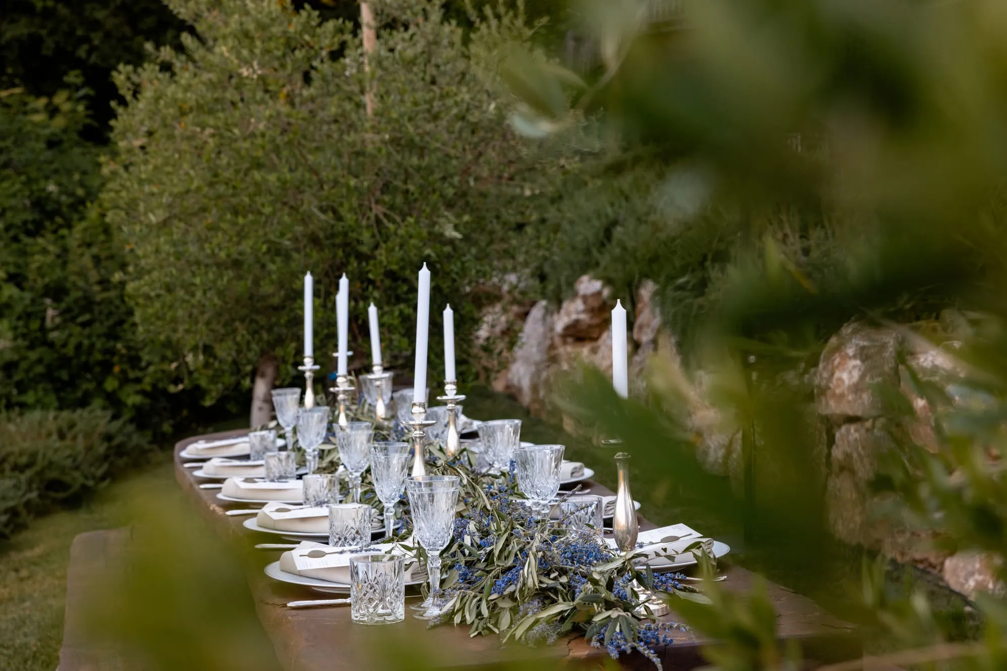 Een lange tafel bij kaarslicht, gezien door het groen