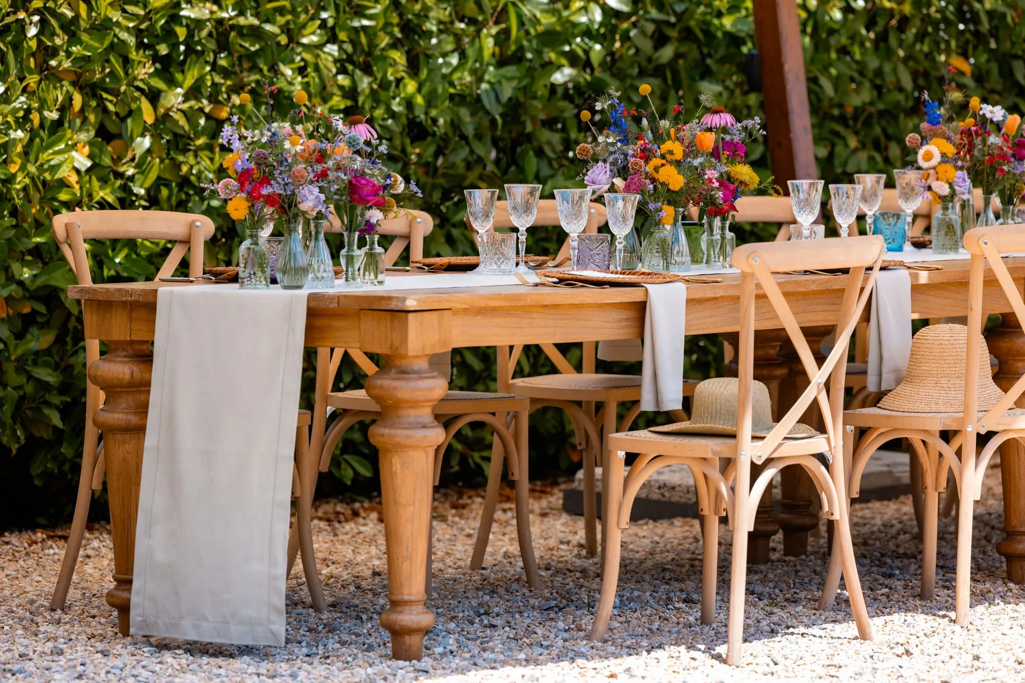 Een lange houten tafel gedekt met kleurrijke bloemen en glaswerk in de tuin