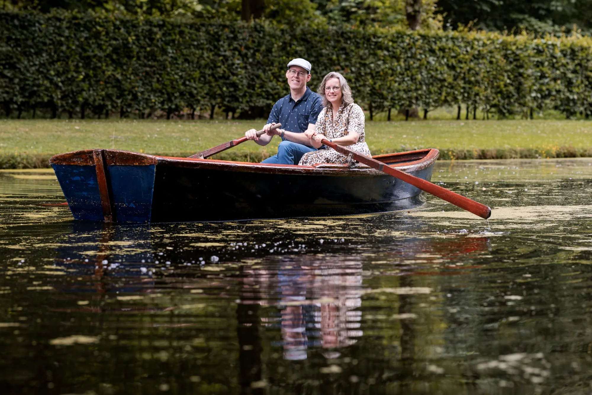 Het stel drijft in de roeiboot op het stille water langs de haag