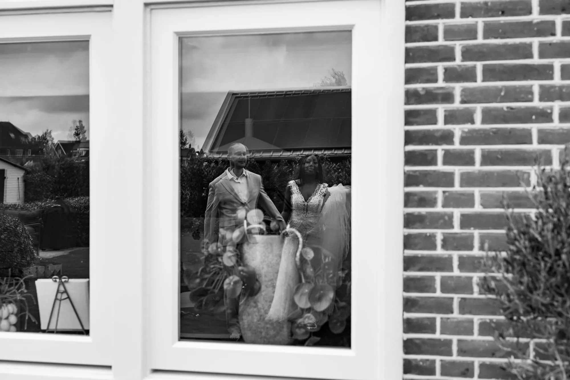 Zwart-witbeeld van het bruidspaar weerspiegeld in het raam van de boerderij