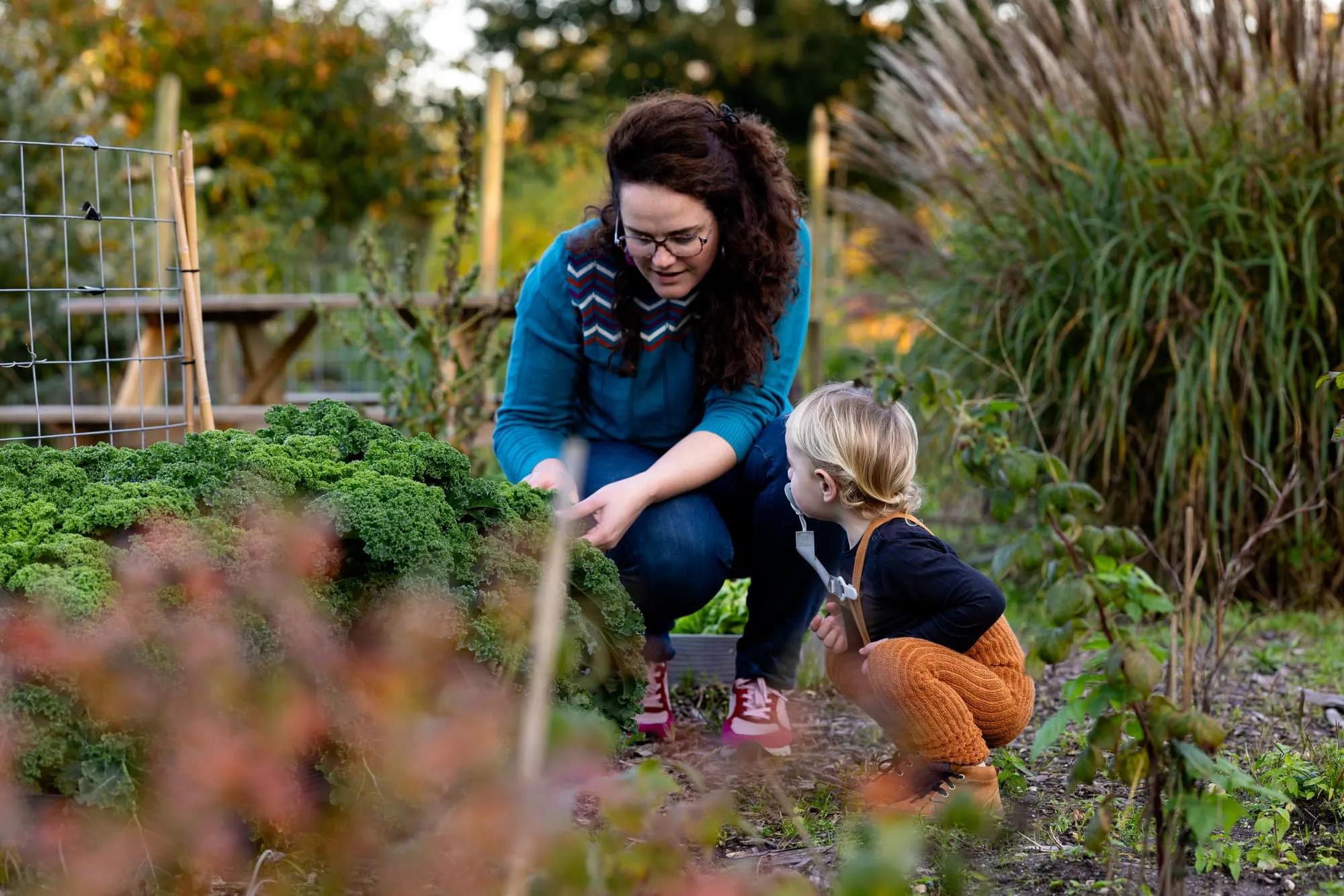 Moeder en dochter hurken samen tussen het groen in de moestuin