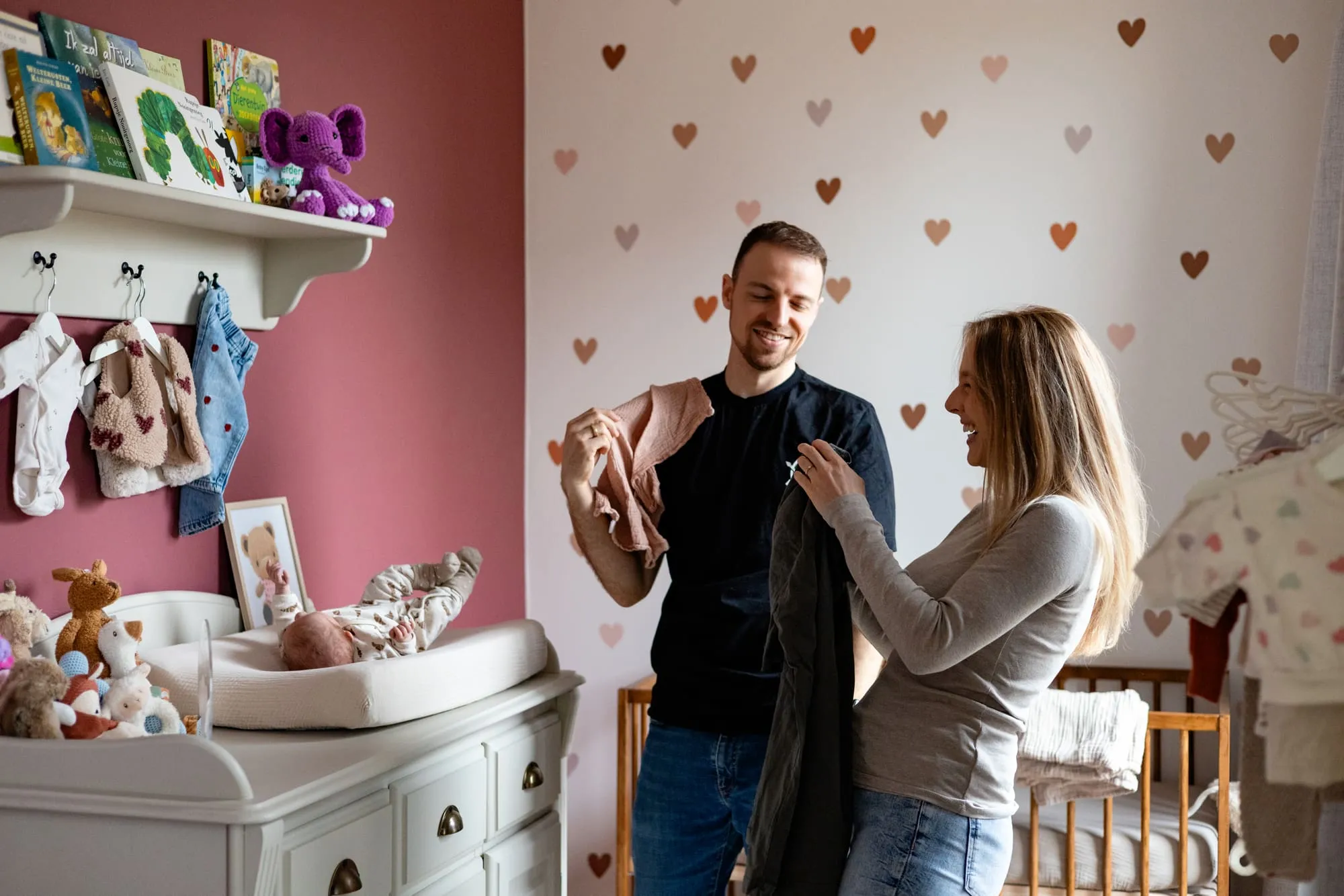 Ouders staan lachend bij het aankleedkussen in de roze babykamer