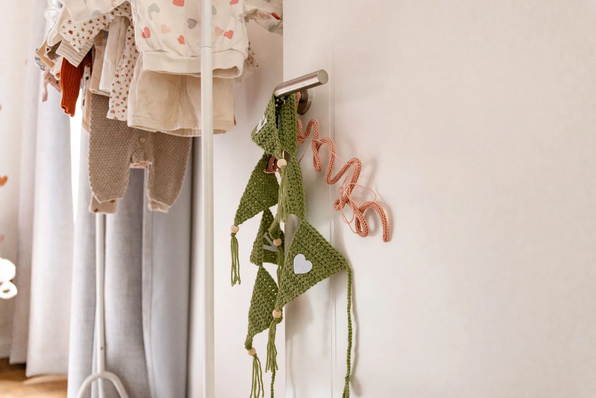 Babykleertjes hangen aan een rek naast een gehaakte slinger