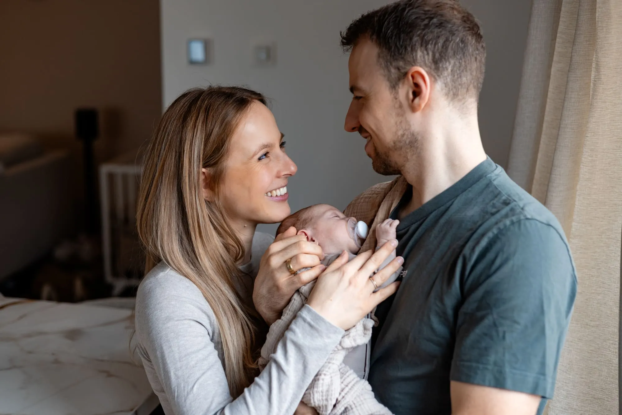 Ouders staan bij het raam met hun baby tussen hen in