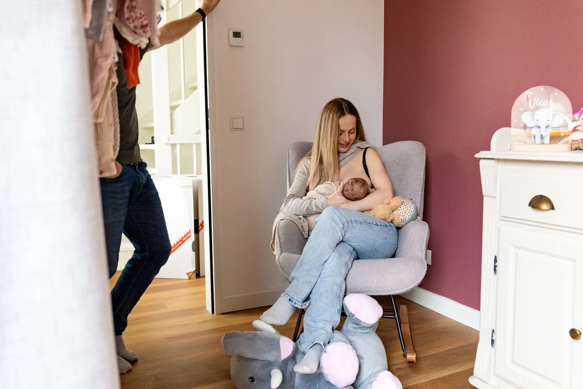 Moeder voedt de baby in een stoel in de babykamer terwijl vader langsloopt