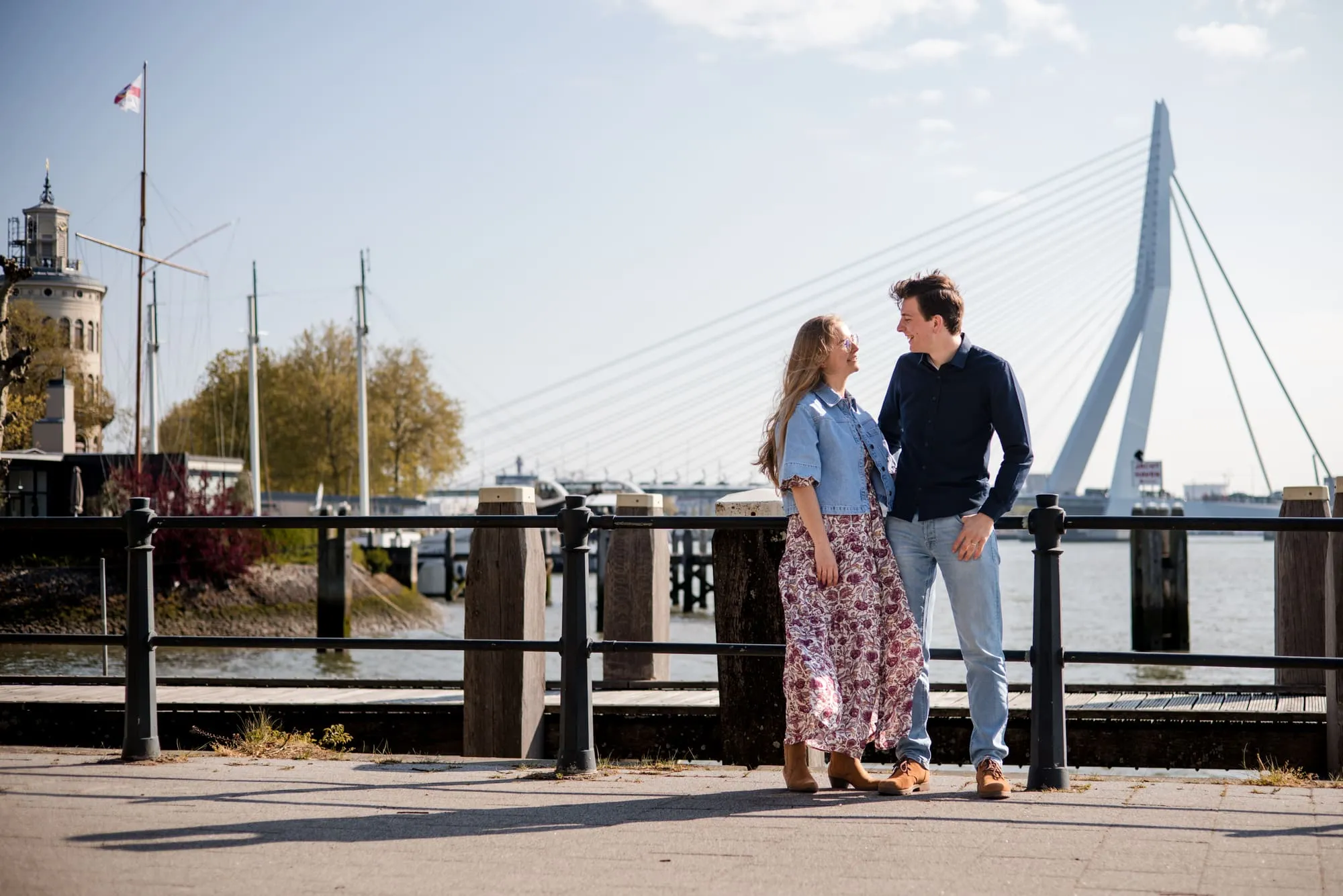 Het stel staat aan de kade tegenover elkaar, met de Erasmusbrug op de achtergrond