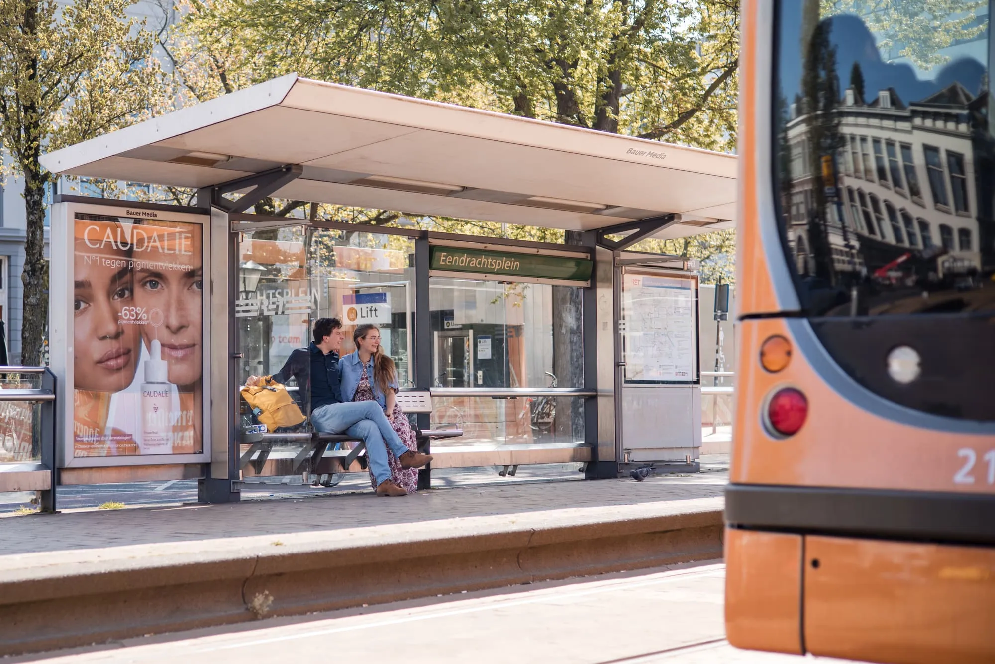Het stel wacht bij de tramhalte terwijl er een tram voorbijrijdt