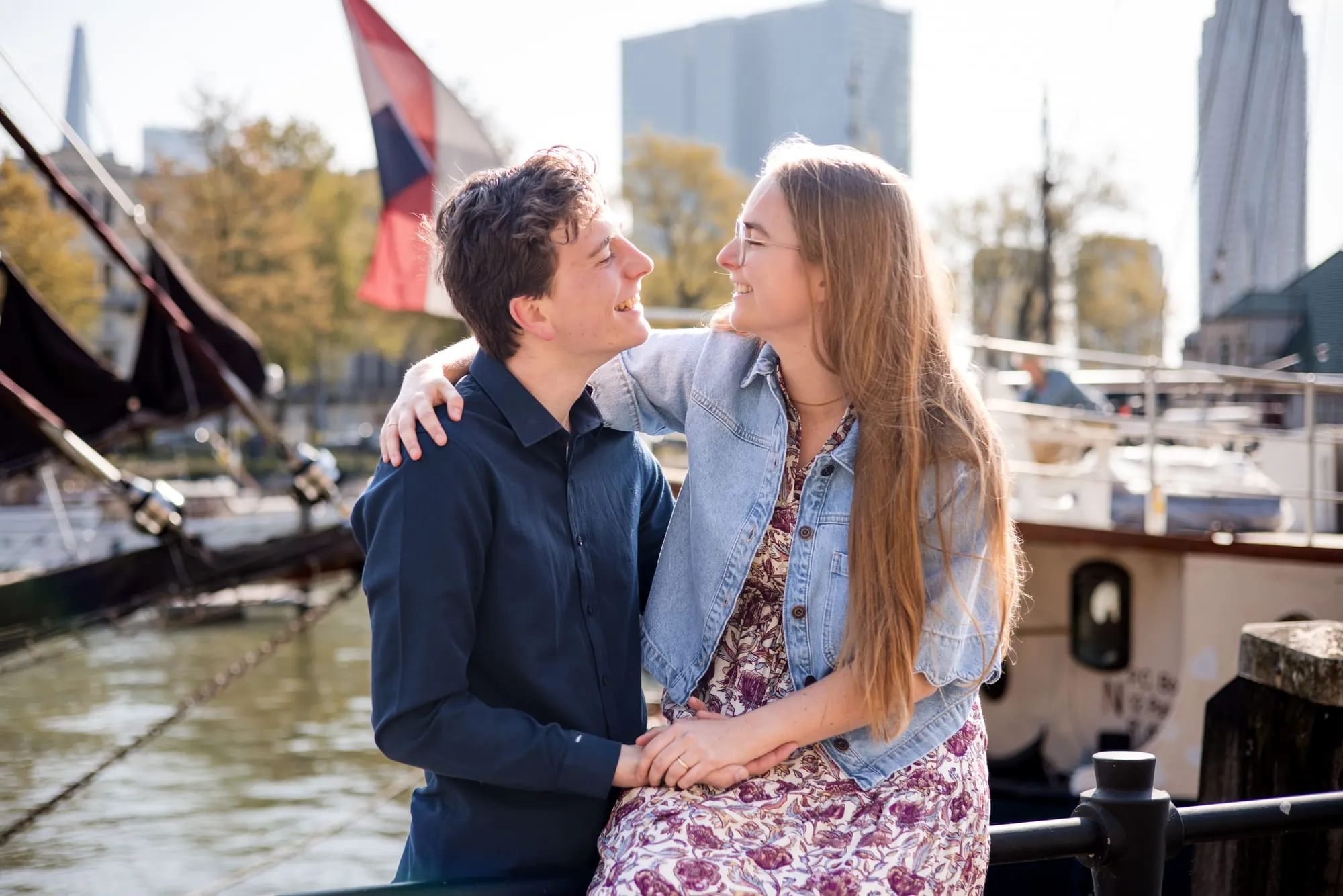 Het stel lacht naar elkaar aan het water, met een wapperende vlag achter hen