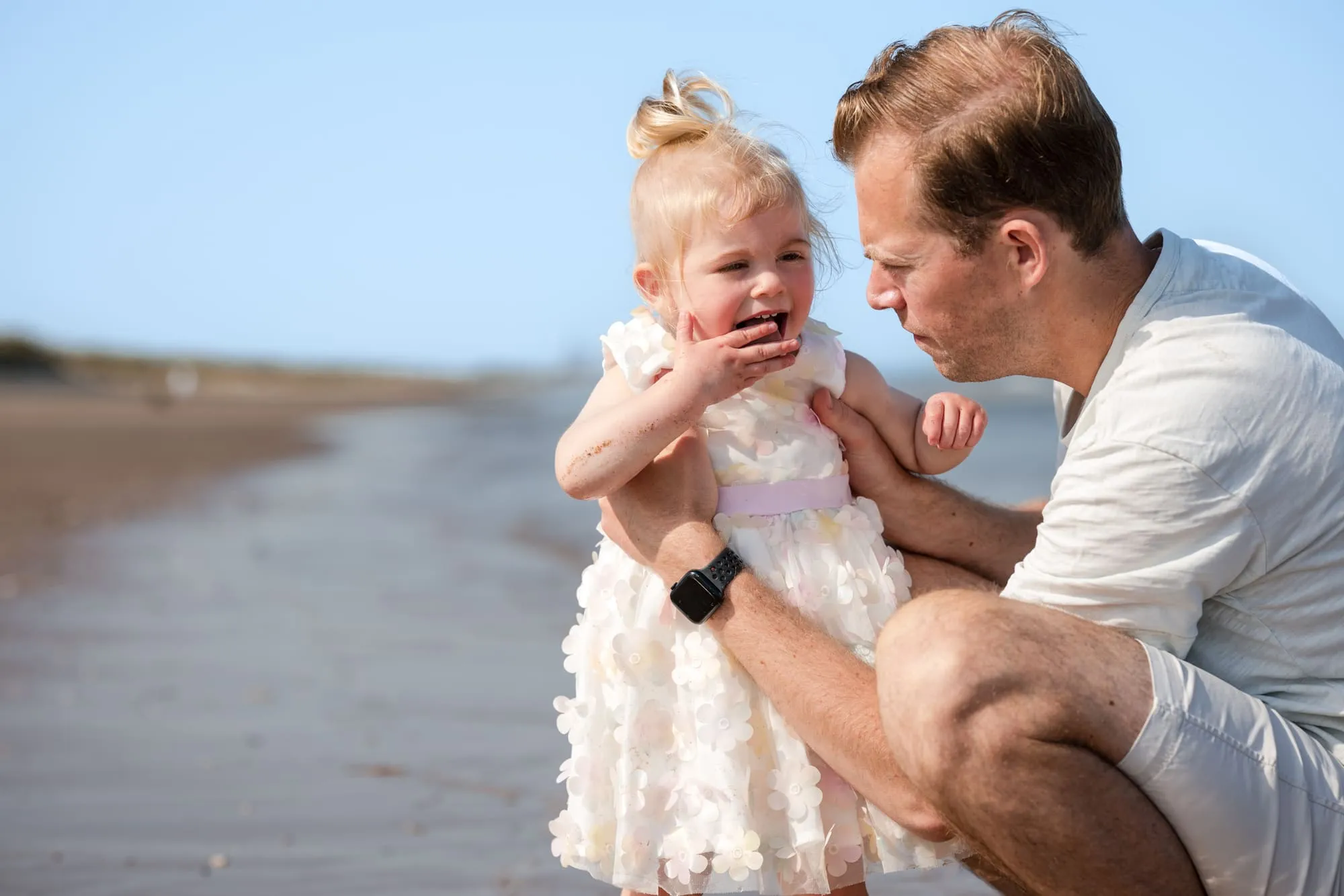 Vader hurkt bij zijn dochter op het strand terwijl ze giechelt