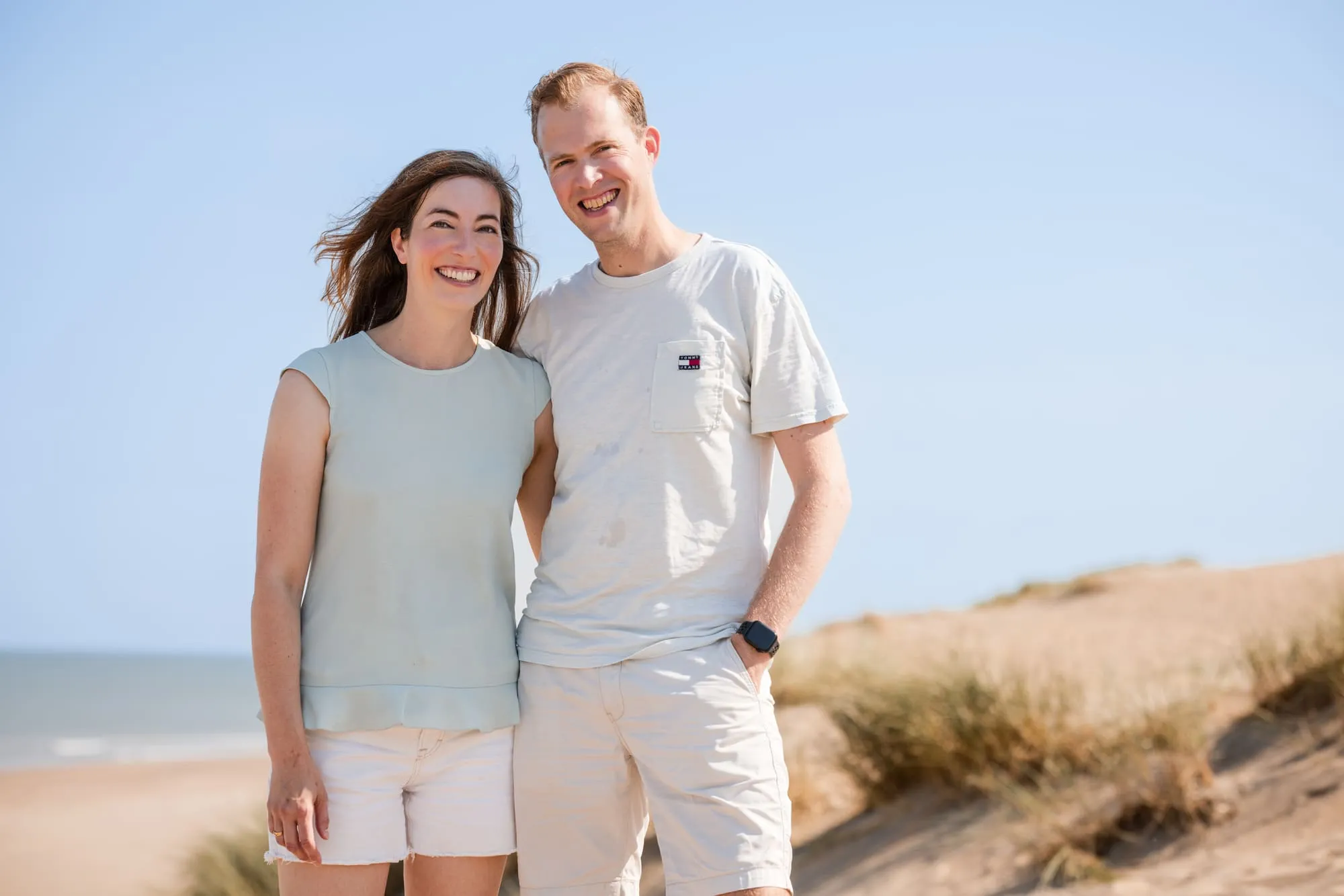 Vader en moeder staan gearmd in de duinen, met de zee achter hen