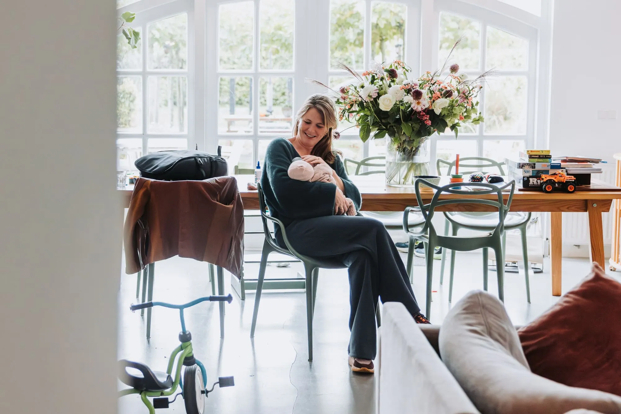 Moeder zit met de baby aan de eettafel bij het raam