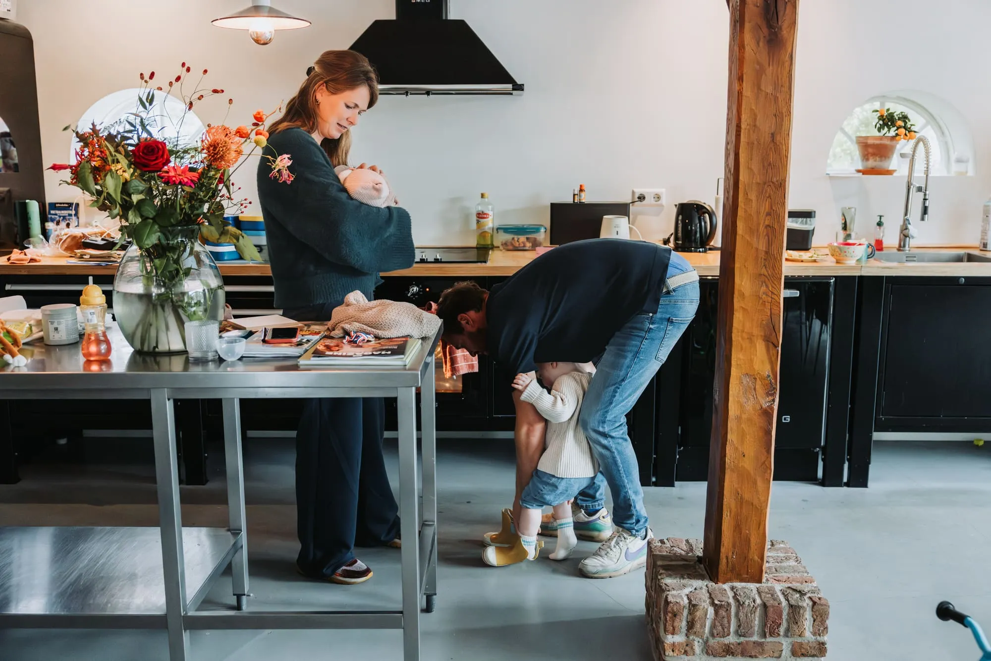 Moeder dekt de tafel terwijl vader zich bukt naar de peuter in de keuken