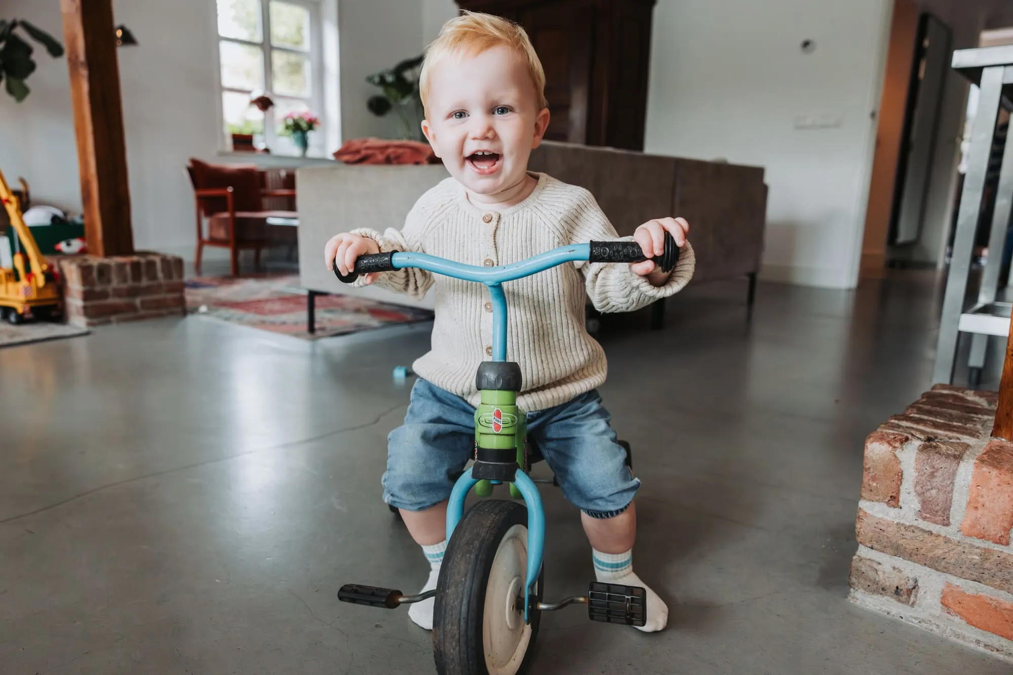 Een peuter rijdt lachend op zijn loopfietsje door de woonkamer